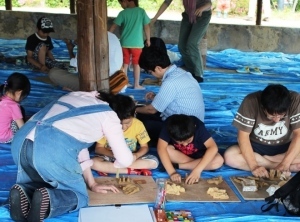 ハニワを作るお父さんと二人の男の子、その男の子にアドバイスするスタッフ