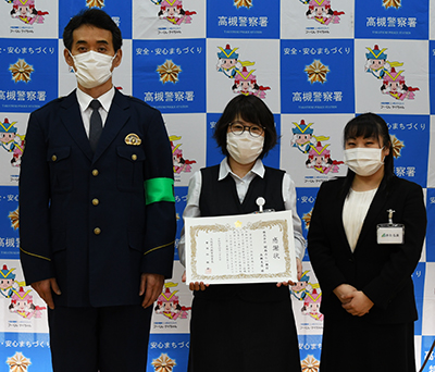感謝状をもつ森永恵子さん（中央）、一緒にうつる林敏郎高槻警察署長（左）と上司の赤羽弘美さん（右）