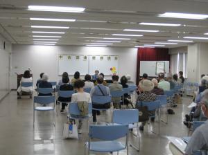 椅子に腰掛けた大勢の市民を前に、演者が朗読している写真