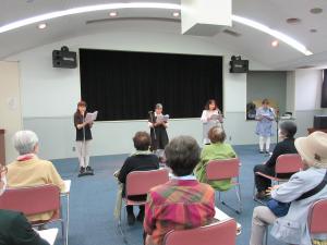 椅子に座った聞き手の人々を前に、4人の朗読者が朗読している写真です。